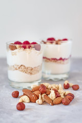 Two glasses of greek yogurt granola with raspberries, oatmeal flakes and nuts on a white background. Healthy nutrition