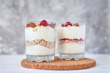 Two glasses of greek yogurt granola with raspberries, oatmeal flakes and nuts on a white background. Healthy nutrition