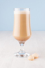 Fresh coffee beverage with cream, biscuits in wineglass in blue interior on white wooden table, vertical.