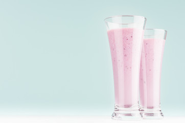 Two fresh purple milkshakes of blueberry closeup on soft light mint color background and white wooden table, copy space.