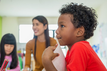African American ethnicity kid with teacher smiling at background in kindergarten classroom..