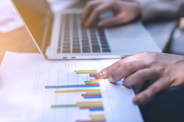 Business women point finger to the graph on paper and another hand type the data on labtop, working outside the office.
