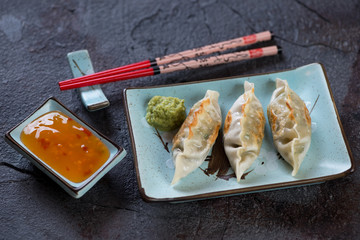 Turquoise plate with pan fried korean dumplings, chopsticks and dipping sauce. Horizontal shot on a grey stone background