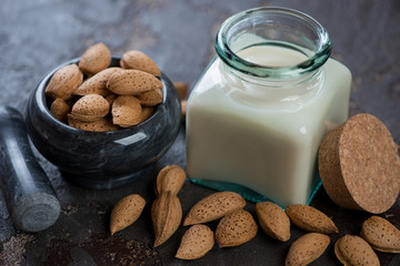 Glass jar with almond milk and unpeeled almond nuts in a marble pounder, studio shot, close-up