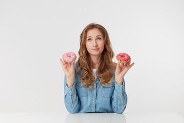 Young beautiful girl holds donuts in her hands, she is dieting, but dreams of eating donuts, imagines what they are tasty and sweet isolated over white background.