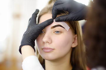 Beautician making depilation with wax strip young woman's eyebrows in spa center.