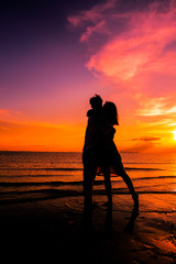 Happy couple silhouettes on the beach at sunset