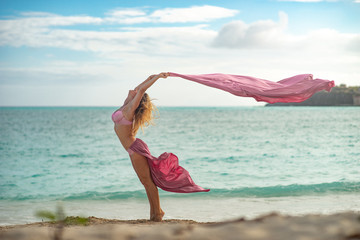 Fit and sporty young girl posing on a beach with pink flying silk