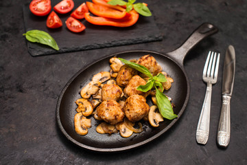 Delicious homemade meatballs served with mushrooms on iron cast pan and fresh vegetables. Side view, selective focus.
