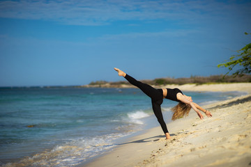 Blond young girl wearing black tights doing dancing poses on the beach. Summer day and happy holiday concept.