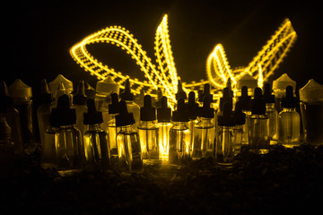 Vape concept. Smoke clouds and vape liquid bottles on dark background. Light effects. Useful as...