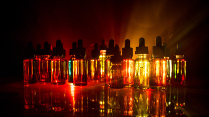 Vape concept. Smoke clouds and vape liquid bottles on dark background. Light effects. Useful as...