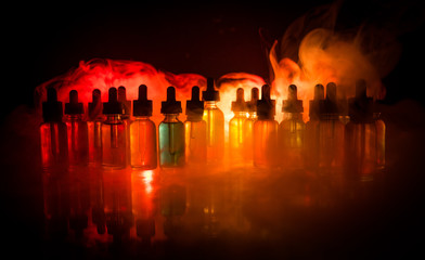 Vape concept. Smoke clouds and vape liquid bottles on dark background. Light effects. Useful as...