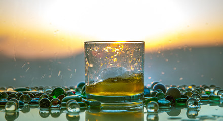 A Glass Of whiskey with ice and gold sunlight. Outdoor shot of whiskey with splash on sunset background.