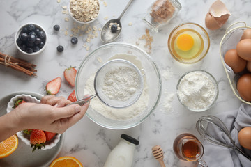 Making pancakes, cake, baking of baker hands pouring or sifting flour in bowl. Concept of Cooking ingredients and method on white marble background. Dessert recipes and homemade.