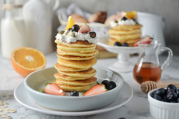 Beautiful dessert, fresh pancakes with blueberries, strawberries, orange, honey and whipping cream on plate. Concept of Cooking ingredients and method and plating, Dessert recipes and homemade.
