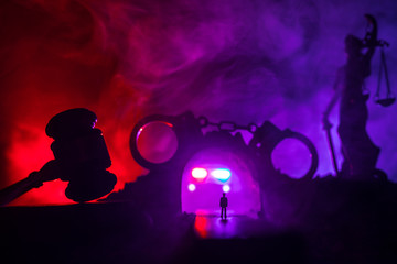 Naklejka na ściany i meble Legal law concept. Silhouette of handcuffs with The Statue of Justice on backside with the flashing red and blue police lights at foggy background. Selective focus