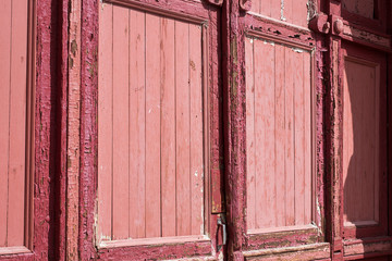 Red old street door with peeled paint in daylight The door is an old wooden red color with peeling paint is illuminated by the bright summer sun 