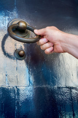 mans hand pulls on brass door knocker, on black wooden door