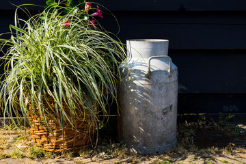 decorative milk churn, can and flower in wicket bucket against black wall