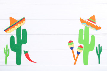 Paper cactuses with hats and maracas on white wooden table