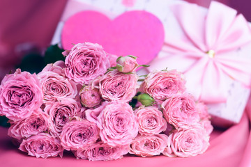 A bouquet of roses and a gift on a pink background