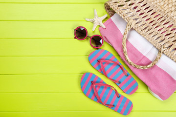 Pair of flip flops with starfish, sunglasses and bag on green wooden table