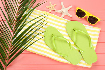 Pair of flip flops with starfishes, sunglasses and palm leaf on coral color background