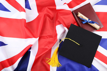 Fototapeta premium Graduation cap with diploma and notepad on British flag background