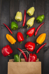 Fresh colored pepper with a paper pack on a  wooden black table. Tasty, useful, set of vegetables to a dark tree. Summer and season product. Green, yellow, red, orange vitamins. Top view