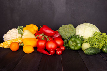 A composition of fresh vegetables on a wooden black table. Tasty colored vitamins on a dark background. A group of useful products. Copy space. 