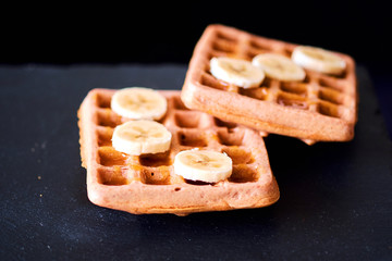 Close-up of waffles with banana and honey on black background