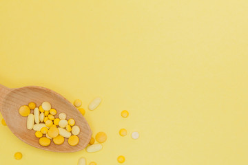 Yellow round vitamin pills in spoon on a yellow background, copy space