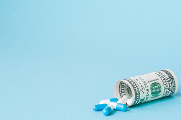 Money dollar rolled up with pills flowing out isolated on blue background, high costs of expensive...