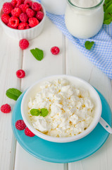 Homemade fresh cottage cheese in a bowl with raspberry berries, sour cream, honey and mint leaves.