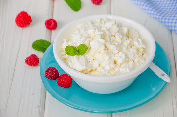 Homemade fresh cottage cheese in a bowl with raspberry berries, sour cream, honey and mint leaves.