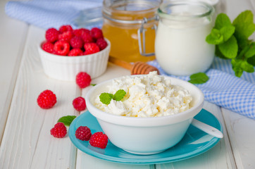 Homemade fresh cottage cheese in a bowl with raspberry berries, sour cream, honey and mint leaves.