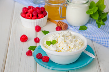 Homemade fresh cottage cheese in a bowl with raspberry berries, sour cream, honey and mint leaves.