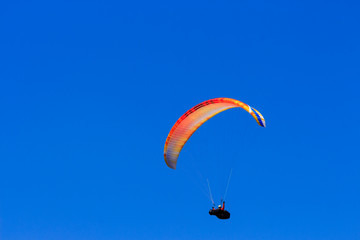 Single colorful paraglider flying in a clear blue sky