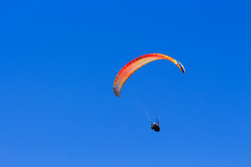 Single colorful paraglider flying in a clear blue sky
