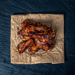 Roasted chicken wings on parchment on a black cement background sprinkled with sesame seeds