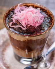 A warm glass of hot chocolate on a white plate with a silver spoon, topped with pink colored fairy floss