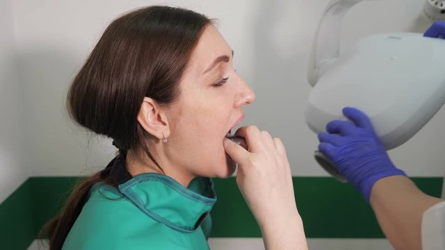 Dentist in gloves prepares young woman to jaw x-ray image in dental clinic, puts a special plate in her mouth, side view.