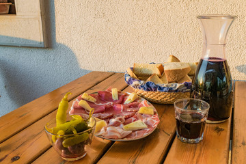 Delicious italian food and drink: red wine accompained by raw ham, salami, cheese and other tasteful cold cuts. All served on a rustic wooden table