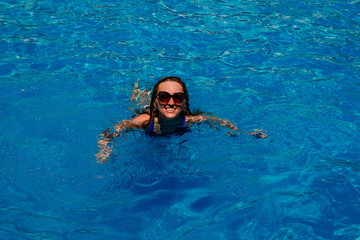 smiling young happy woman swimming in the pool with blue water.