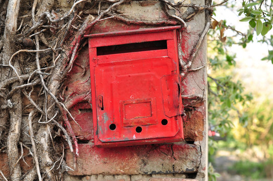Old beautiful red mail box on a wall is intertwined with wood