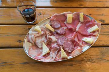 Delicious italian food and drink: red wine accompained by raw ham, salami, cheese and other tasteful cold cuts. All served on a rustic wooden table