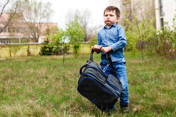 a small child picks up a huge heavy backpack on the green grass