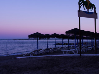 Calm evening scene at a beach in Spain's resorts, Empty beds, straw umbrellas, purple colors.