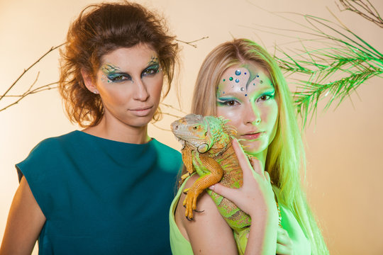Wild animal in the hands of man. Two girls with an unusual make-up and with an iguana in their hands. Animal out of it. An image of a female predator and snake